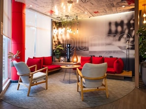 A modern lounge area with red sofas, wooden chairs, a small table, and a decorative plant.
