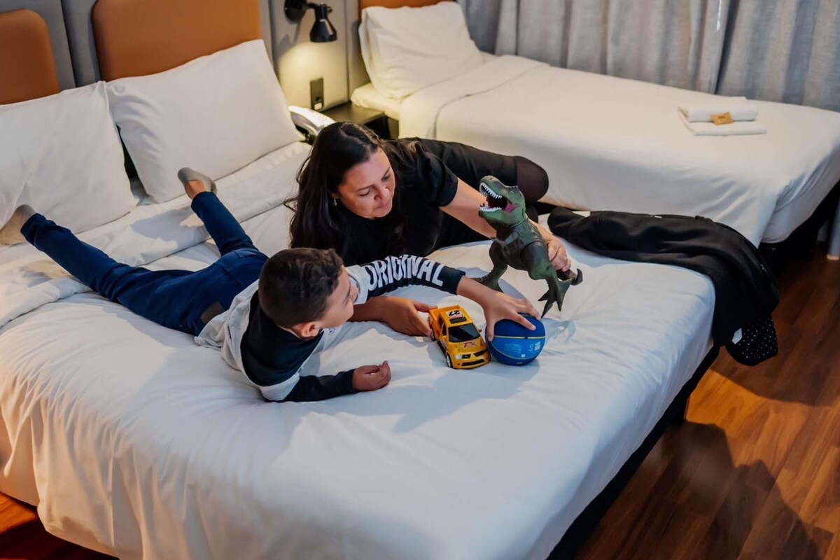 A hotel room with two beds, a nightstand with a lamp, and a toy dinosaur.