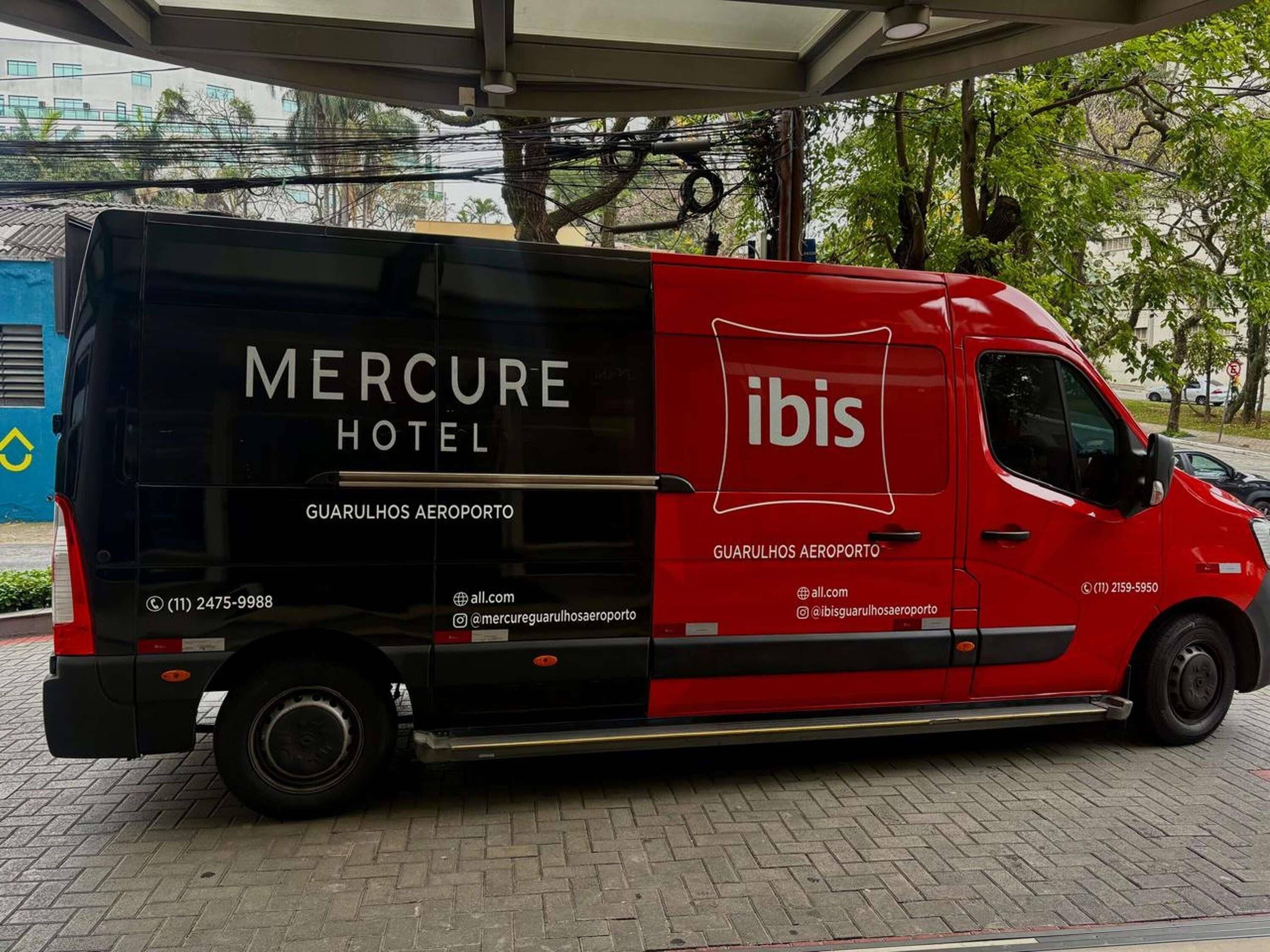 Una furgoneta de reparto roja y negra con la marca 'Mercure Hotel' e 'ibis', estacionada en un aeropuerto.