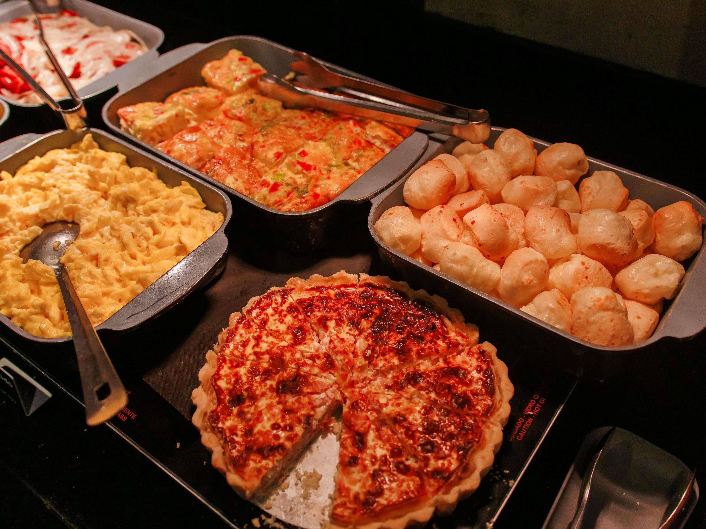A buffet with various dishes including scrambled eggs, a baked casserole, shrimp, and a pie.
