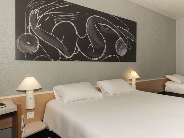 Una habitación de hotel con una cama, dos lámparas de noche, una obra de arte colgada en la pared y una mesita de noche con lámpara.