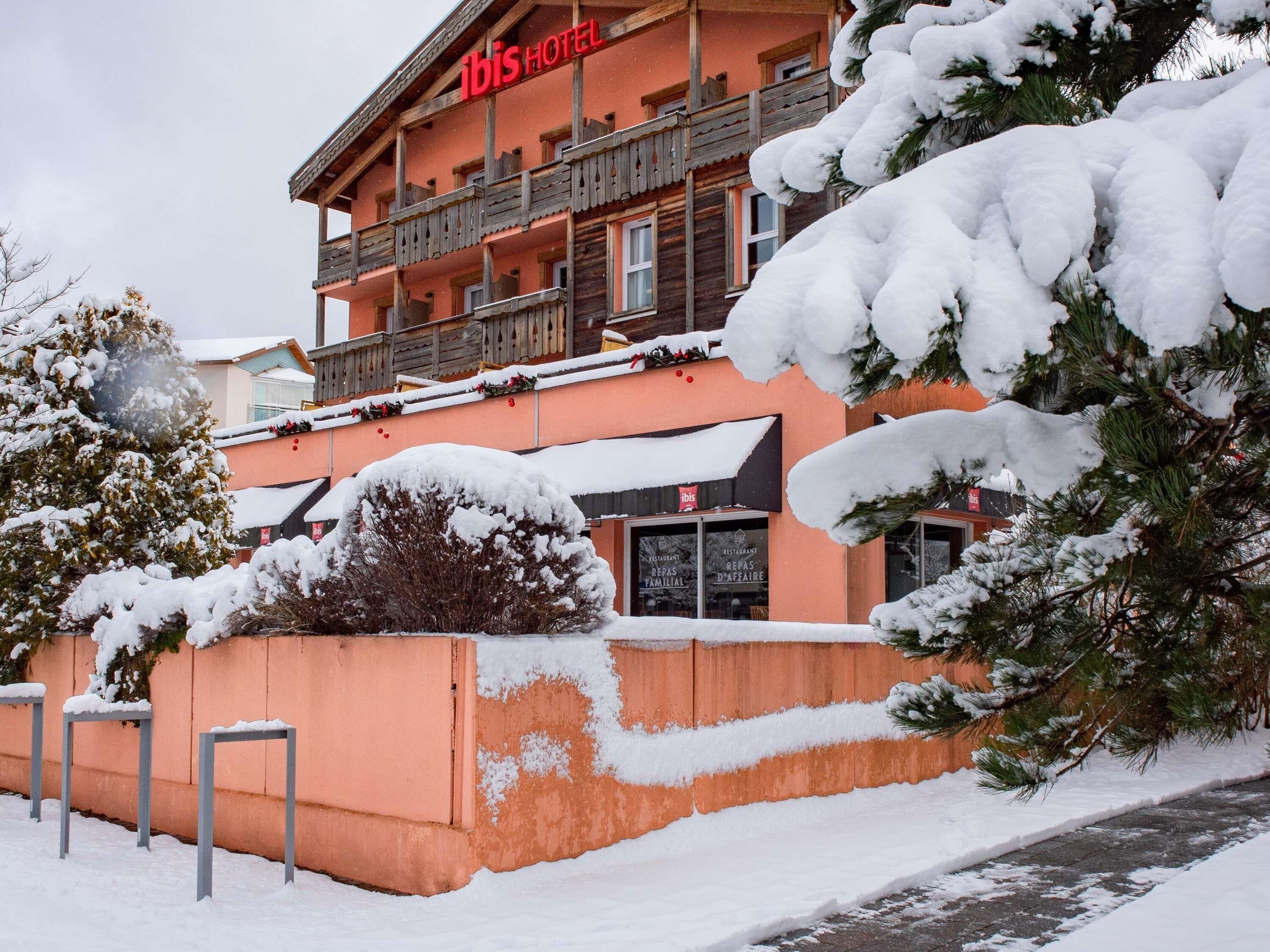 Un hôtel doté d’un balcon en bois, d’arbres couverts de neige et d’un ciel dégagé.