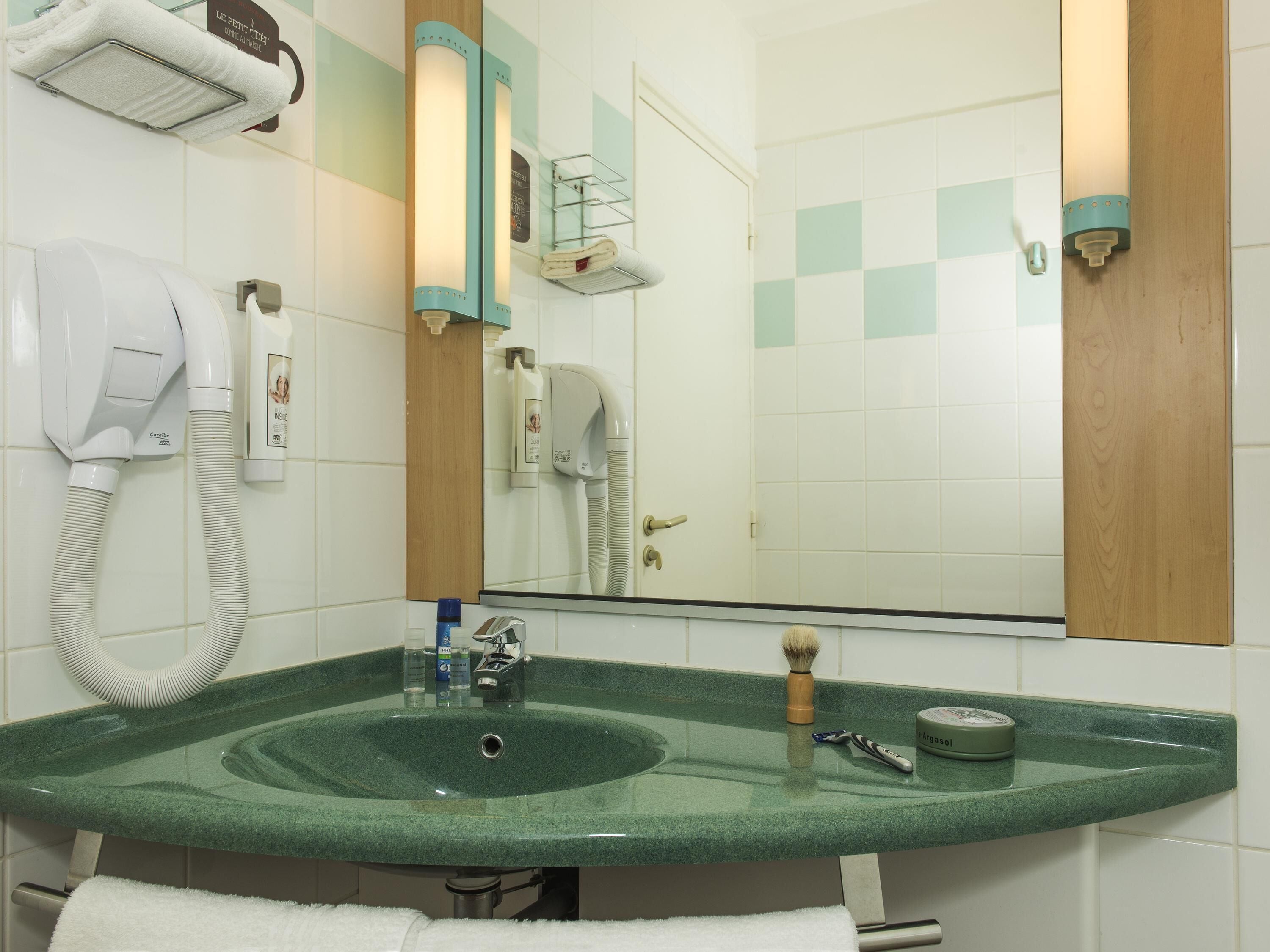 A bathroom with a green sink, a mirror, a hairdryer, and a towel rack.