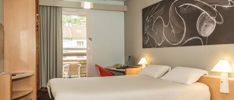 Habitación de hotel con cama, escritorio con lámpara, una silla, armario y un cuadro abstracto grande en la pared.