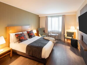 A hotel room with a bed, bedside tables, a chair, a small table, a TV, and a window with curtains. - Mercure Porto Gaia Hotel (Vila Nova de Gaia)