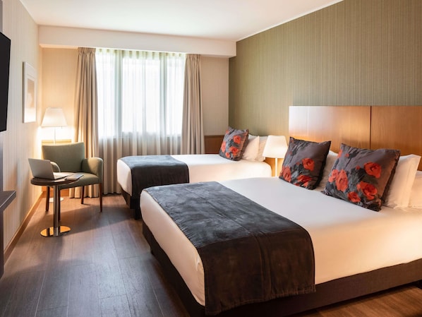 Habitación de hotel con dos camas, un escritorio con una computadora portátil, una silla y un televisor.