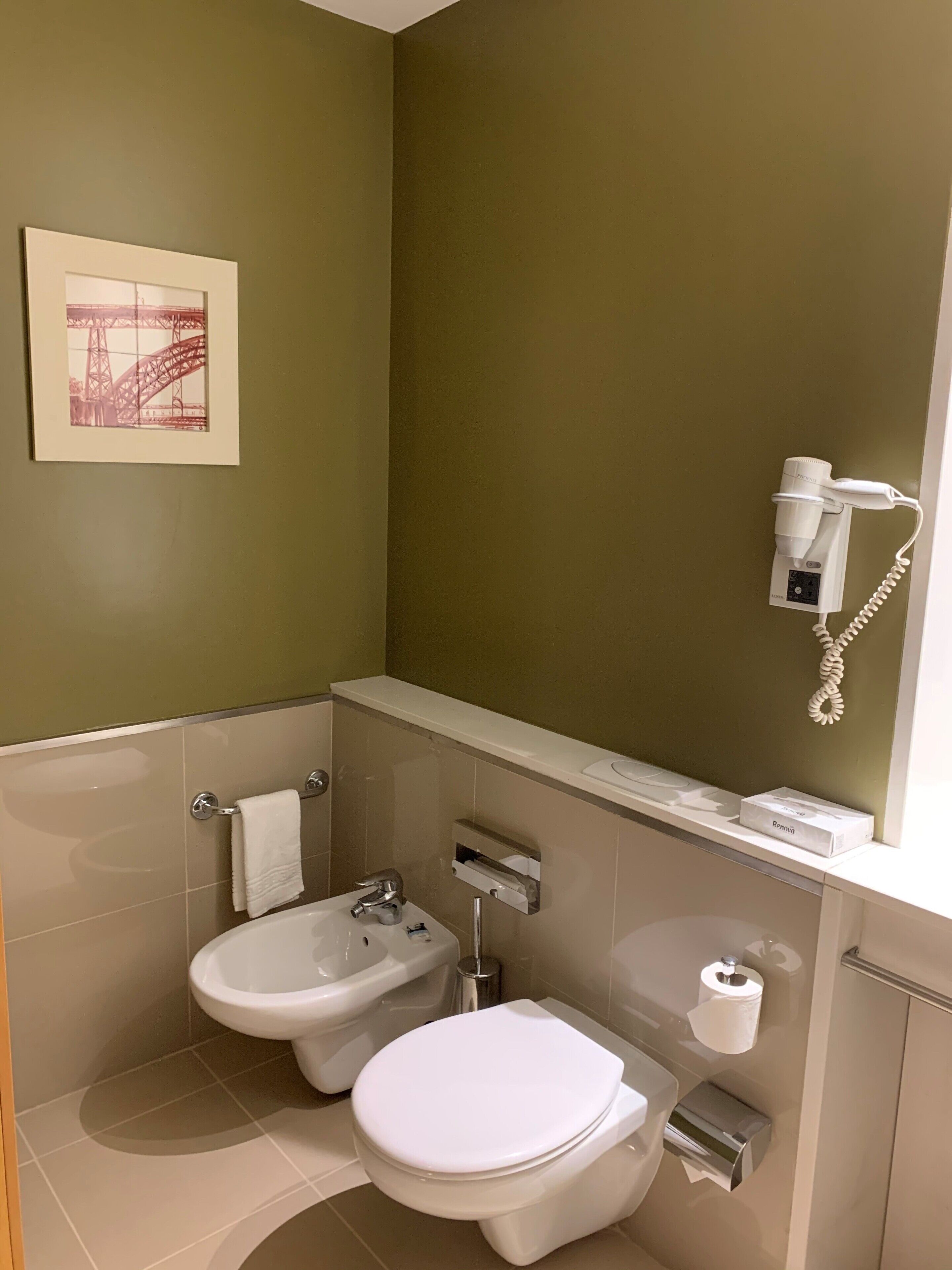 Een badkamer met toilet, bidet en een aan de muur gemonteerde haardroger.