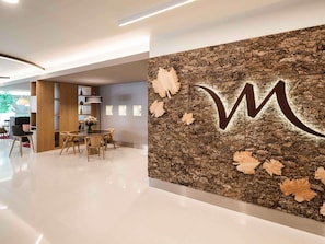Un interior moderno con una recepción, un comedor y una pared con textura y una gran letra 'M'.