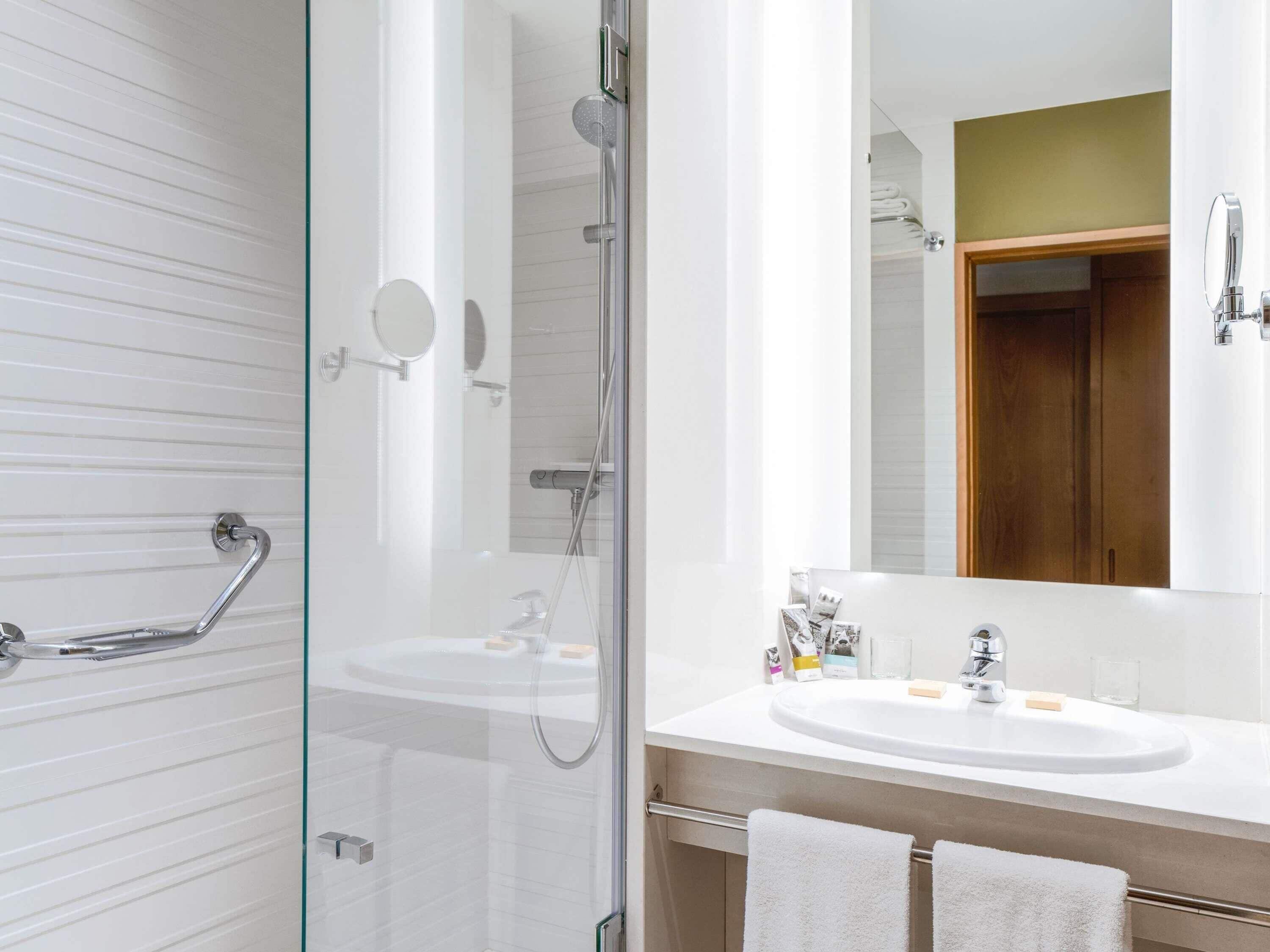 A modern bathroom with a glass-enclosed shower, a white sink with a mirror, and a wooden door.