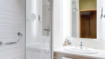 Un baño moderno con ducha envuelta en vidrio, un lavamanos blanco con espejo y una puerta de madera.