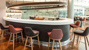 Zona de bar moderna con una barra curva, taburetes y una variedad de botellas y copas.