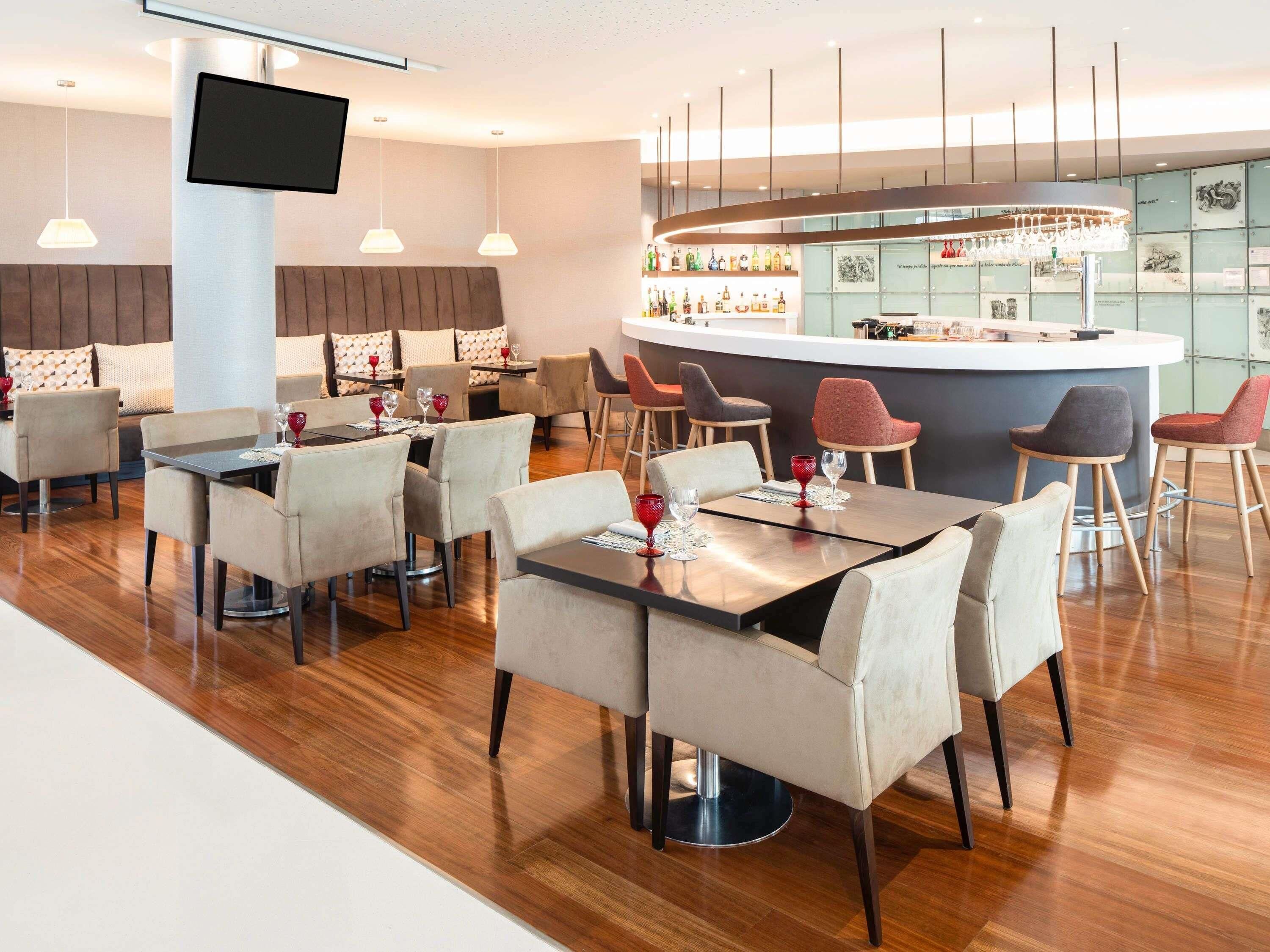 Um restaurante moderno com área de bar, piso de madeira e mobiliário contemporâneo.