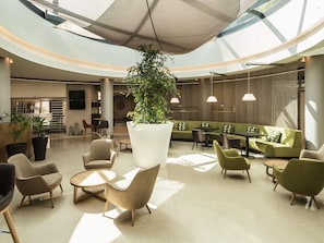 A spacious lobby with a central plant, seating areas, and a modern design. - Mercure Porto Gaia Hotel (Vila Nova de Gaia)