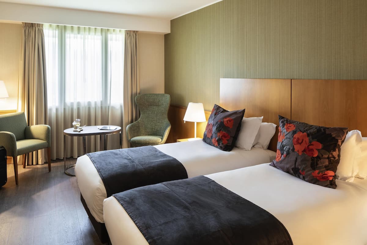 Ein Hotelzimmer mit zwei Betten, einem Sessel, einem kleinen Tisch und einer Lampe.