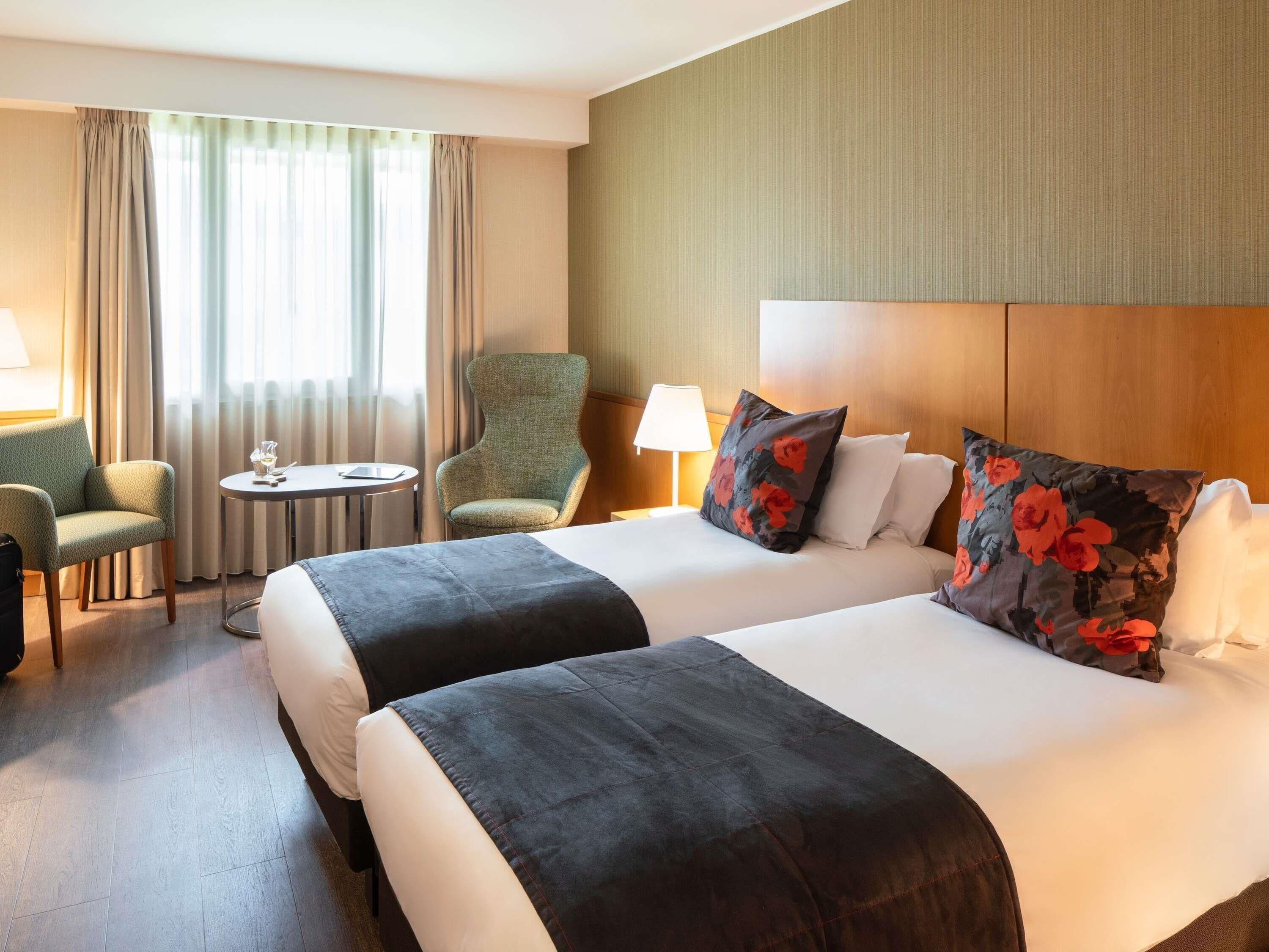 Habitación de hotel con dos camas, una silla, una mesita y una lámpara.