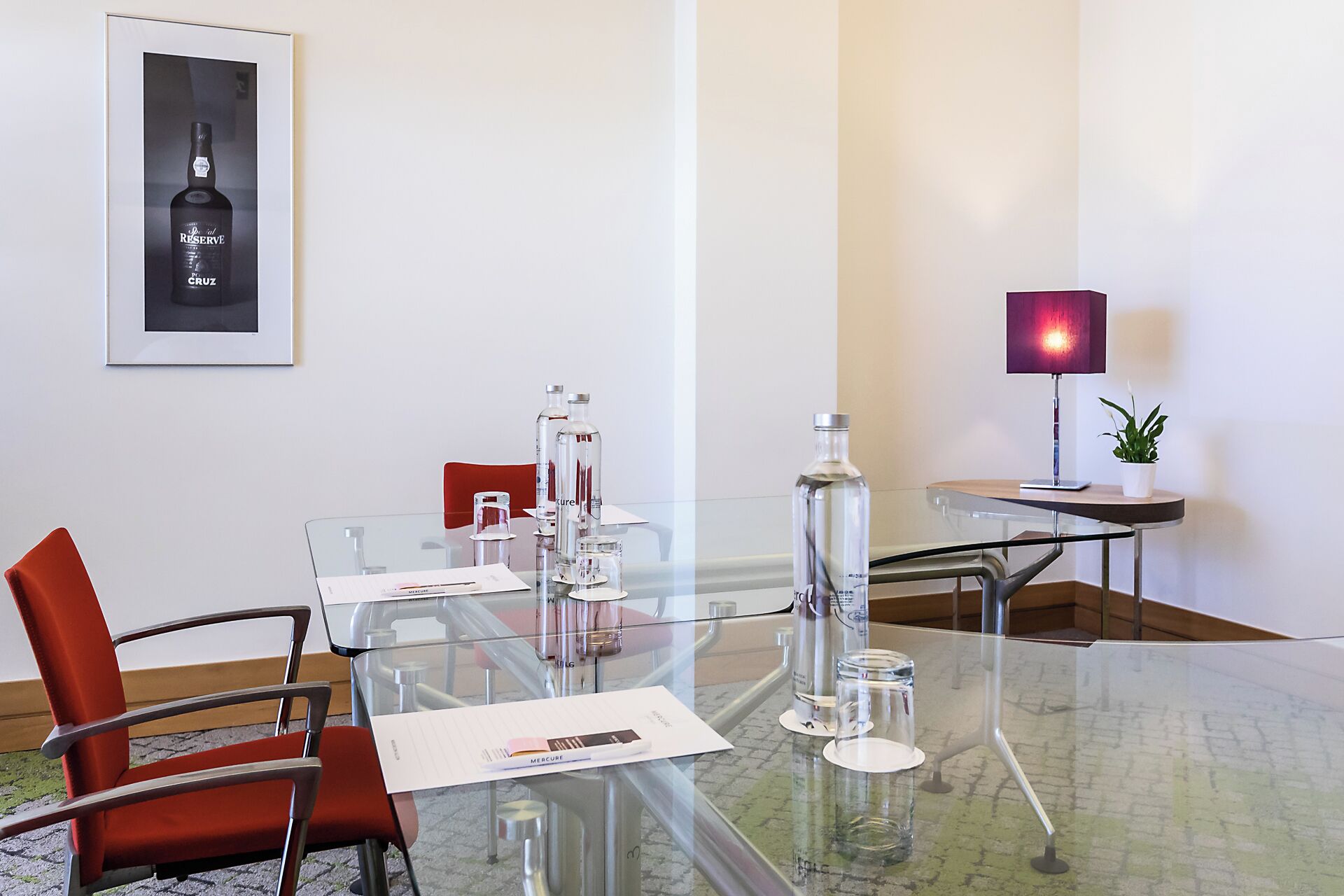 A modern conference room with a glass table, clear glass chairs, and a framed picture on the wall.