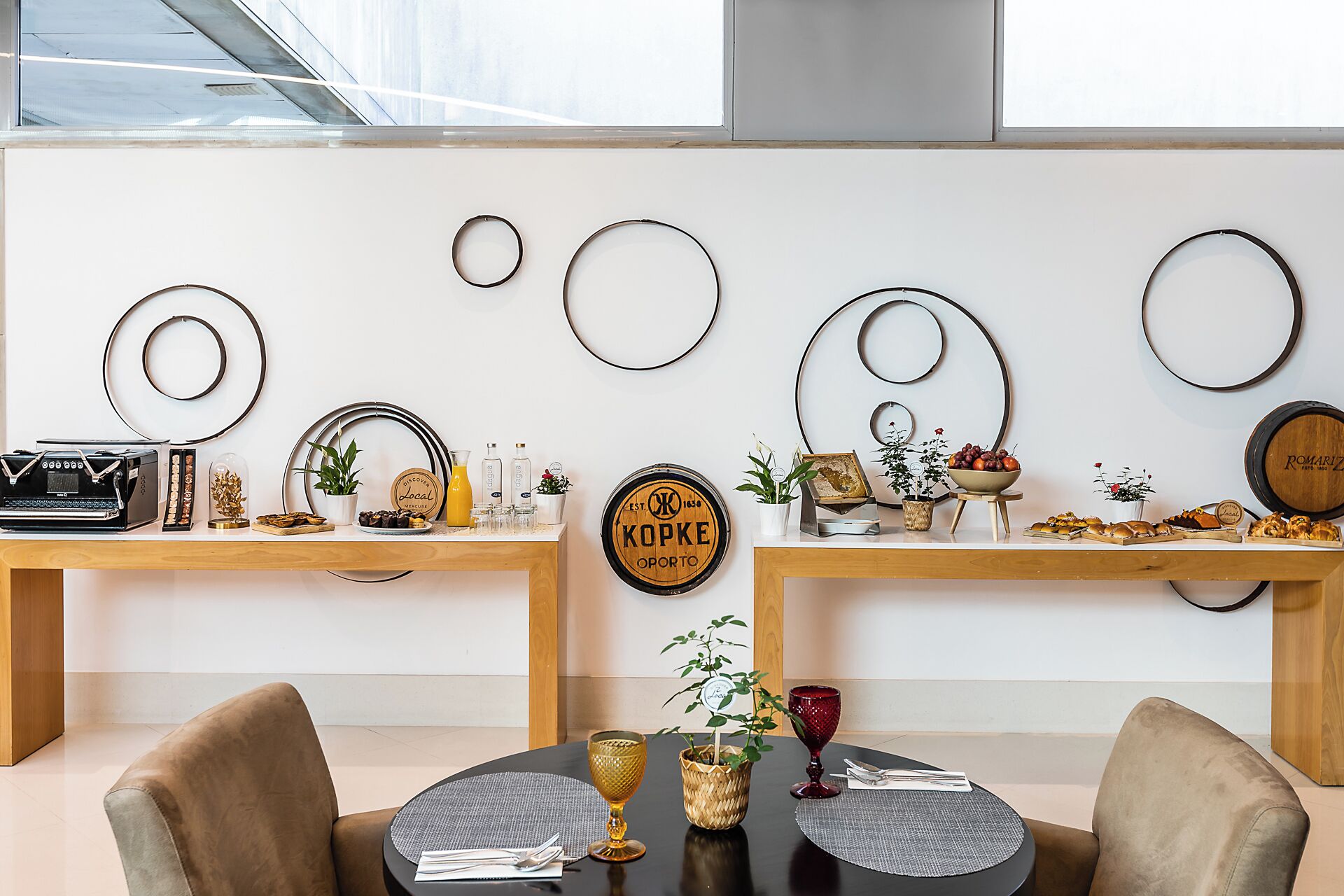 A modern dining area with two wooden tables, each with a variety of food items and decorative elements.