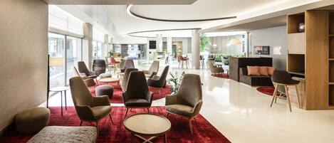 A modern lobby with seating areas, a reception desk, and a large window providing natural light.