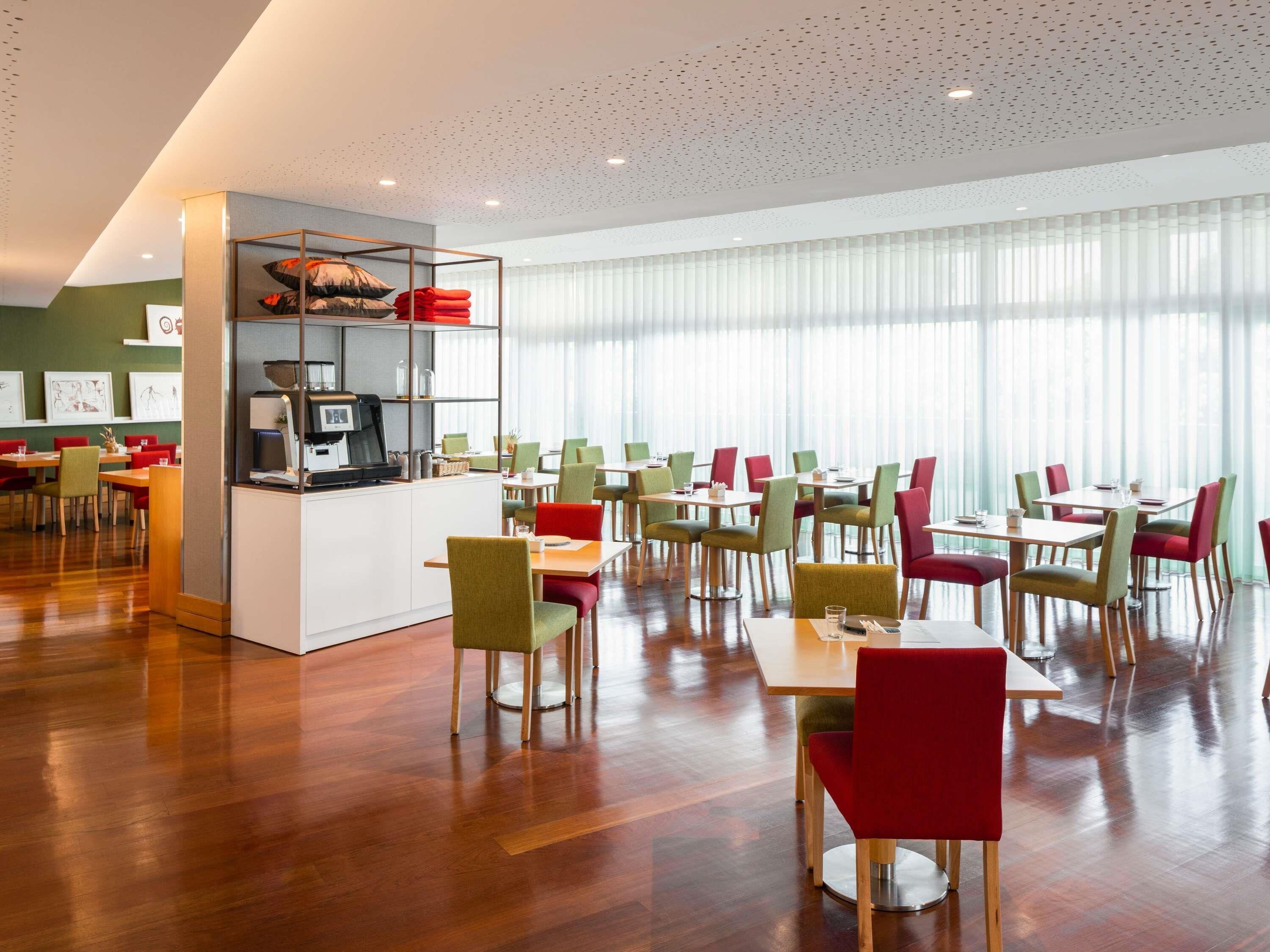 A modern dining area with wooden flooring, a central counter with a coffee machine, and multiple tables and chairs.