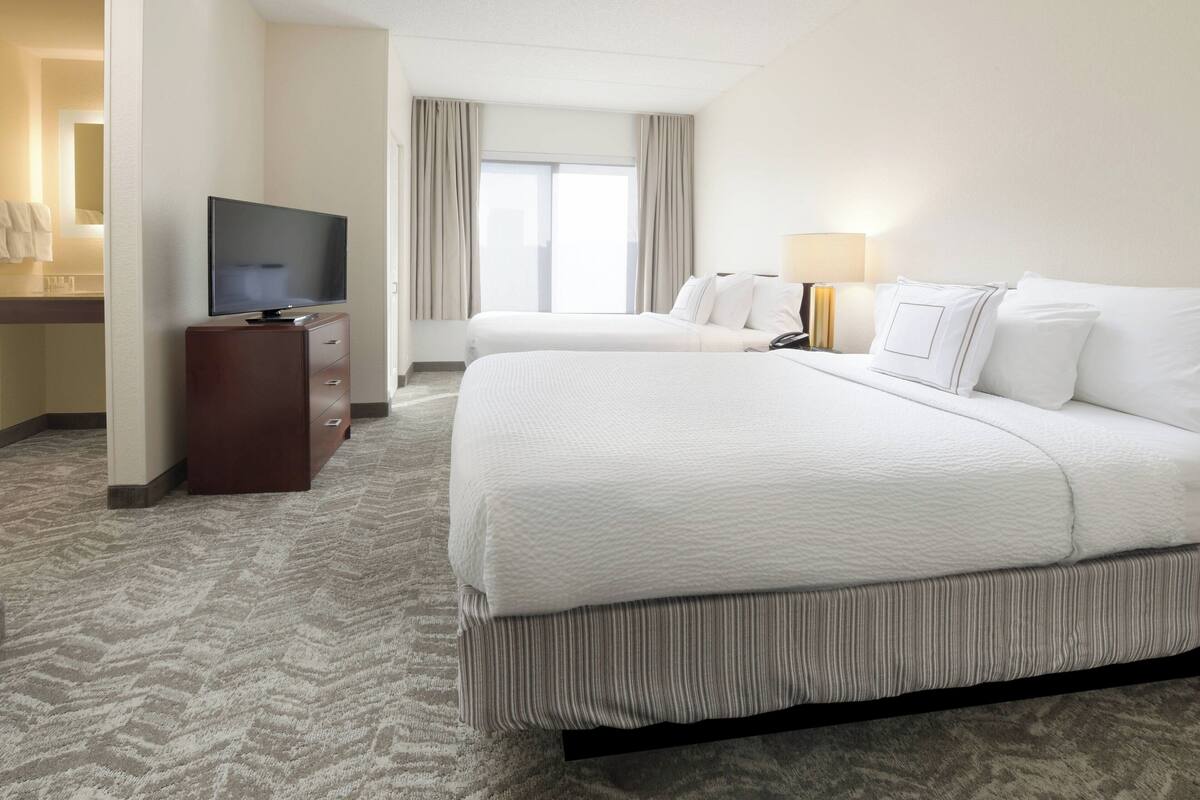 A hotel room with two beds, a TV, a desk, and a window with curtains.