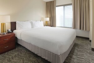 Una habitación de hotel con una cama grande, dos lámparas de noche, una mesita de noche de madera y una ventana con cortinas.