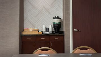 A hotel room with a wooden table, two chairs, a coffee maker, and a door with a keyhole.