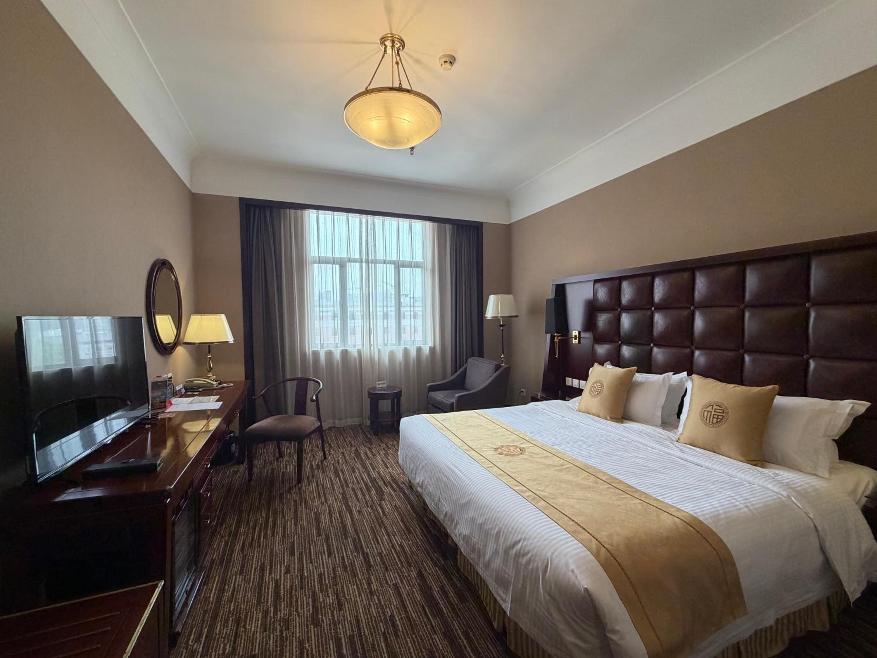 Una habitación de hotel con una cama grande, televisión, escritorio y una silla.