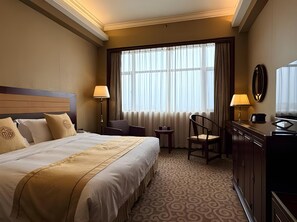 Ein Hotelzimmer mit einem großen Bett, einem Schreibtisch, einem Stuhl und einem Fenster mit Vorhängen.