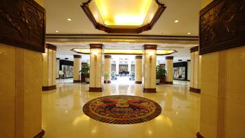 A spacious lobby with a central decorative rug, tall columns, and a large illuminated ceiling fixture.