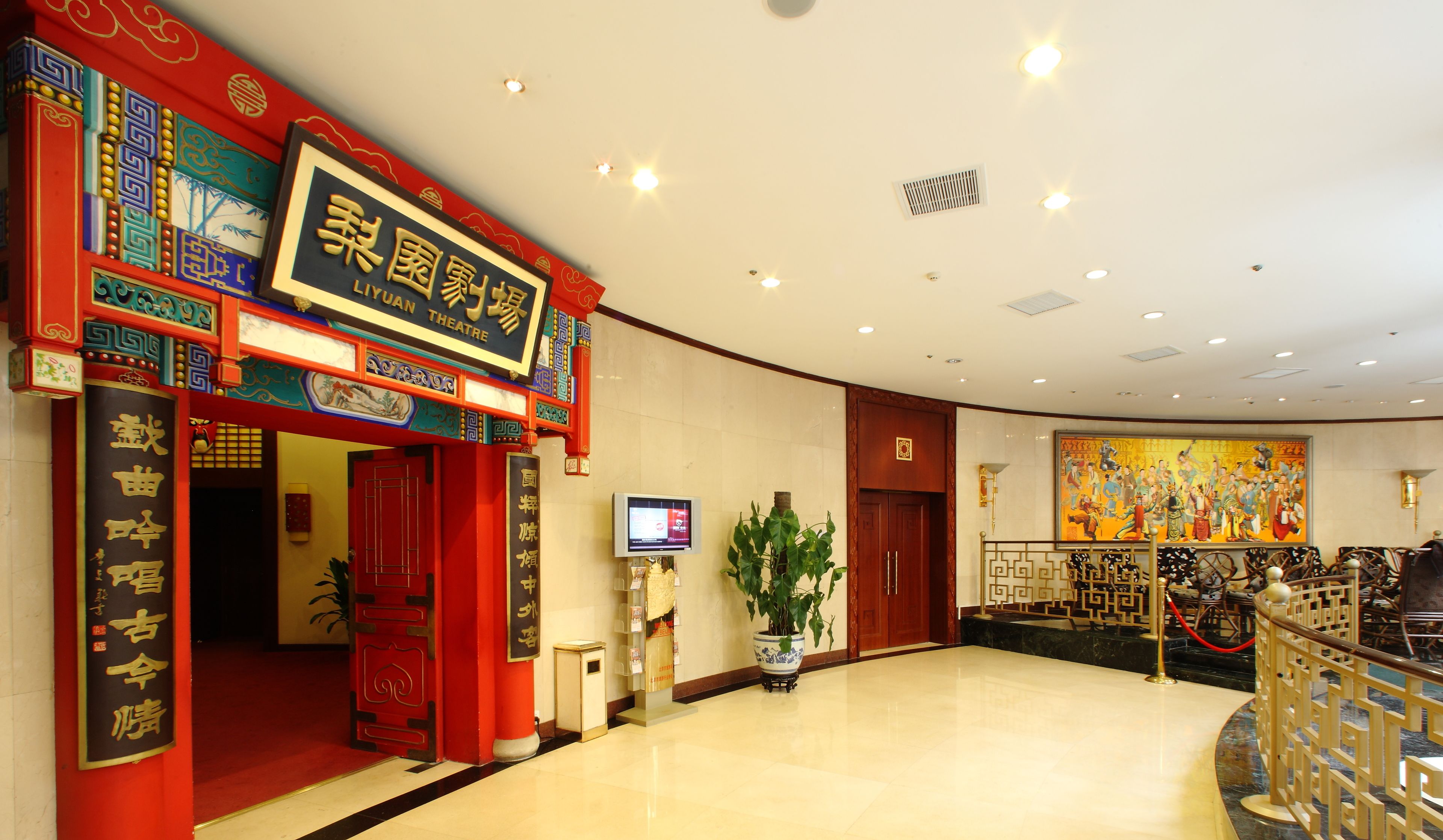 Un teatro chino tradicional con ornamentadas decoraciones rojas y doradas, un gran mural y una pantalla digital moderna.