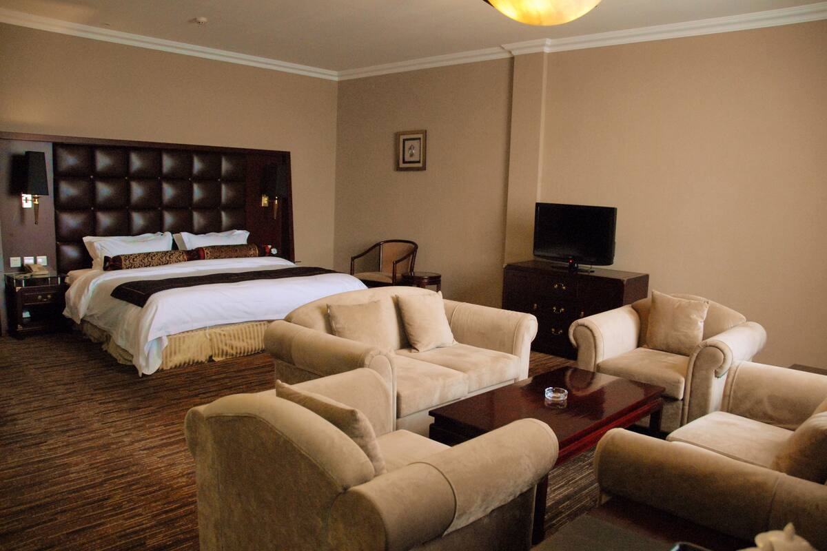 A hotel room with a large bed, two sofas, a coffee table, a TV, and a framed picture on the wall.