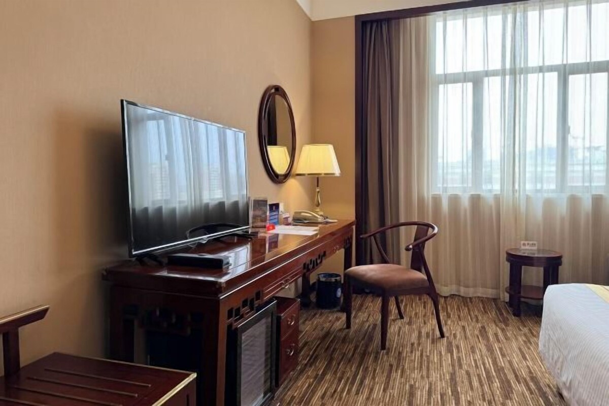 Ein Hotelzimmer mit Fernseher, Schreibtisch, Stuhl, Lampe und einem Bett.
