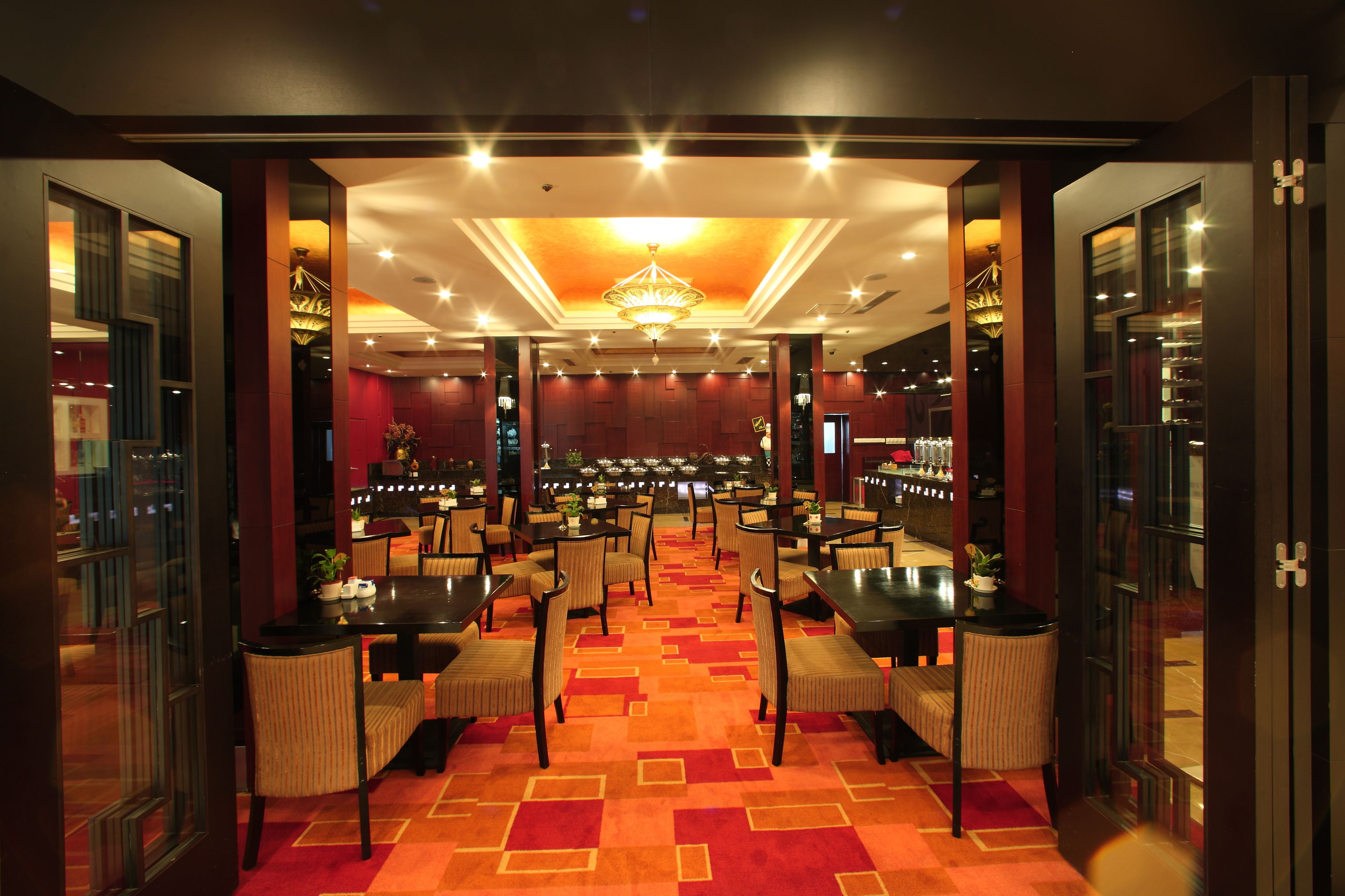A hotel lobby with multiple tables and chairs, a central chandelier, and a patterned carpet.
