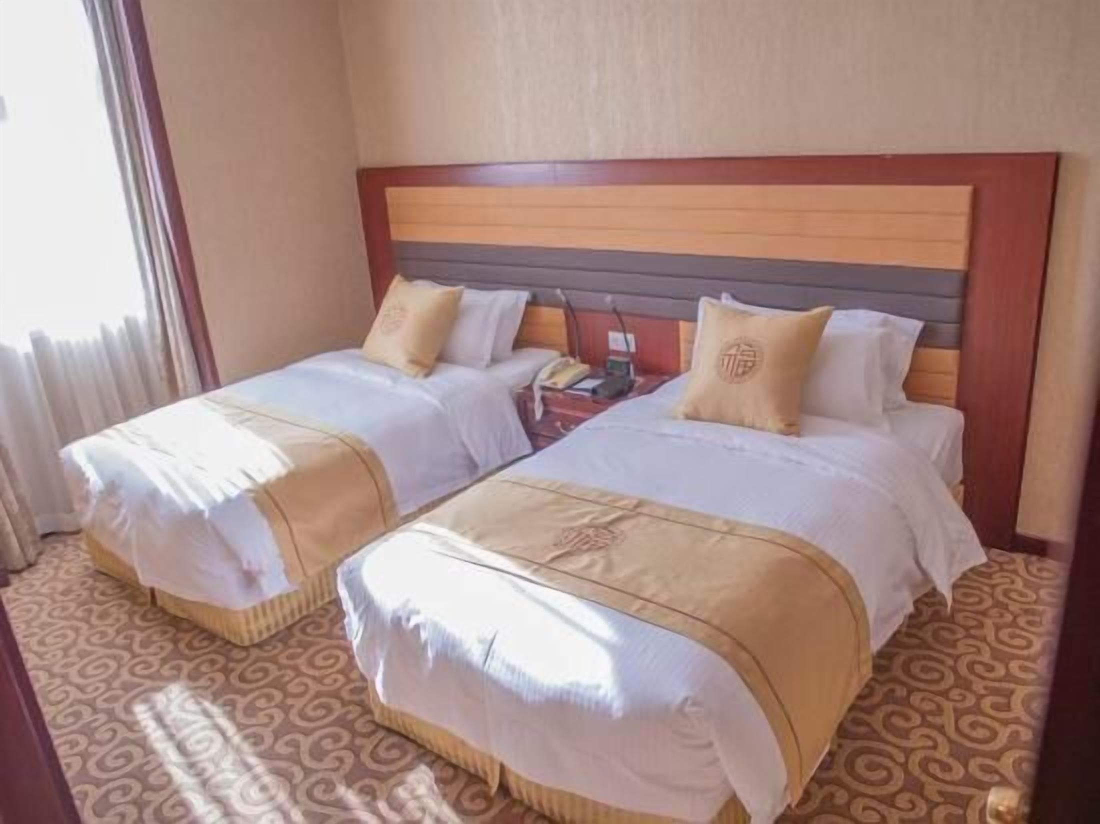 A hotel room with two beds, each with a wooden headboard, white bedding, and beige throw blankets.