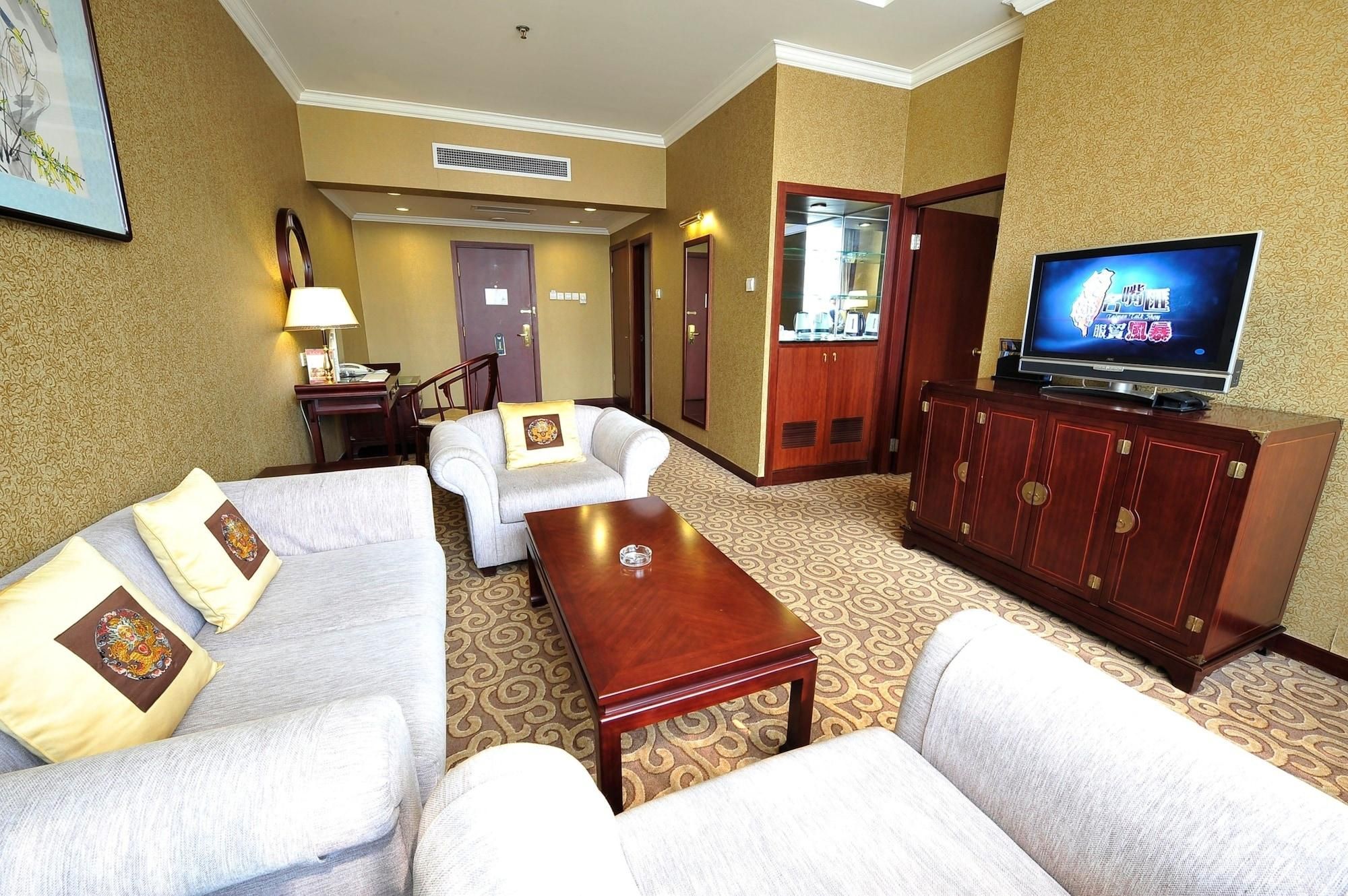 A hotel room with a TV, two sofas, a coffee table, a desk, and a wardrobe.