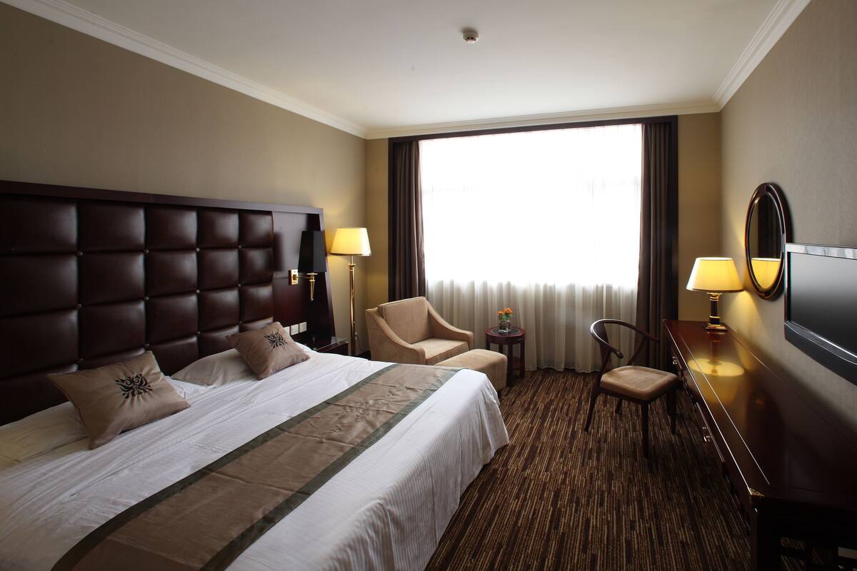 A hotel room with a large bed, a desk with a TV, a chair, and a window with curtains.