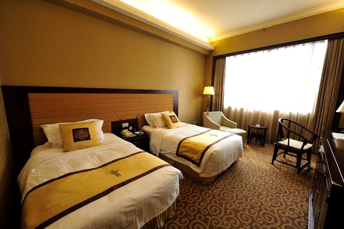 A hotel room with two beds, a desk, a chair, and a large window with curtains.
