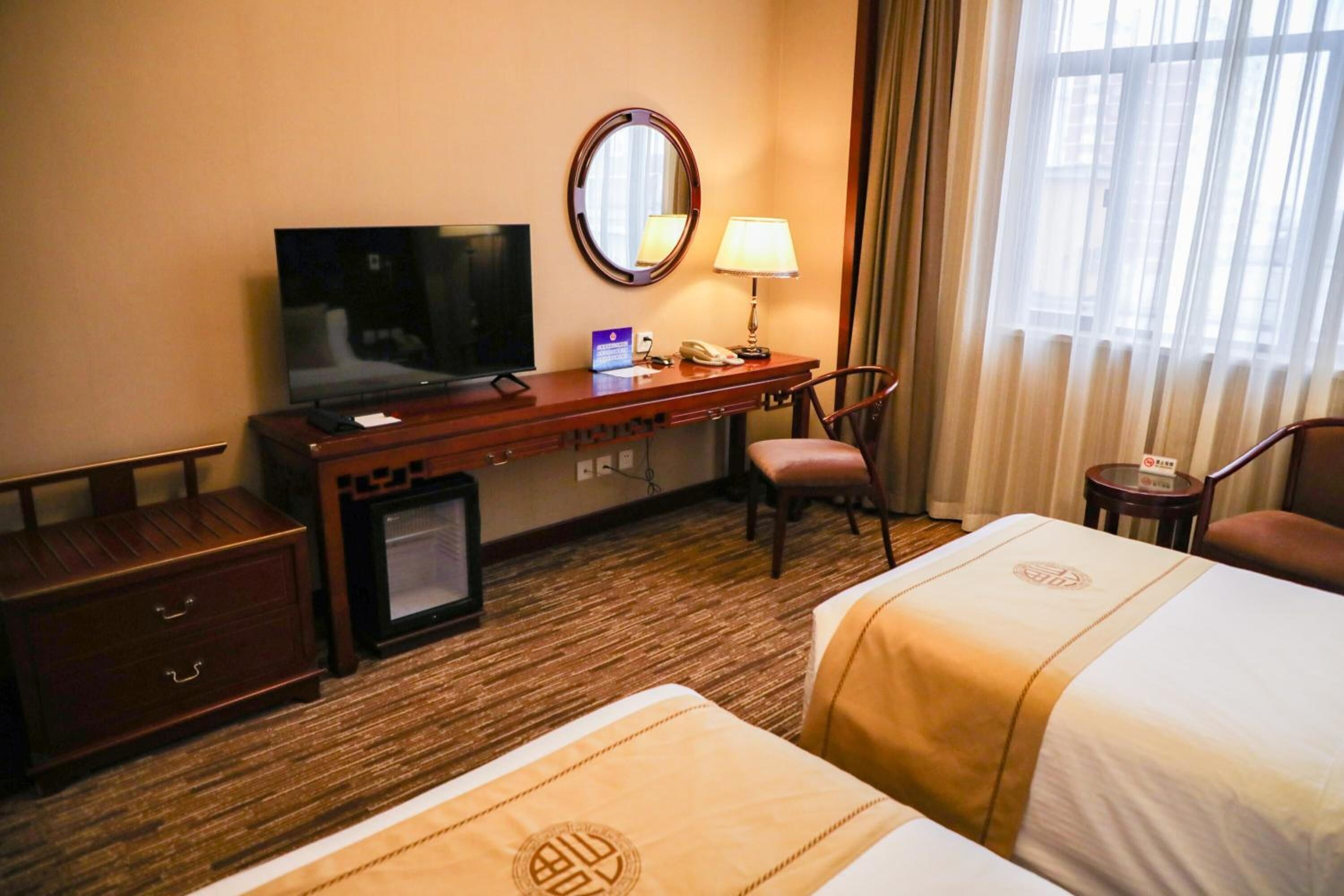 A hotel room with a TV, desk, chair, and two beds.