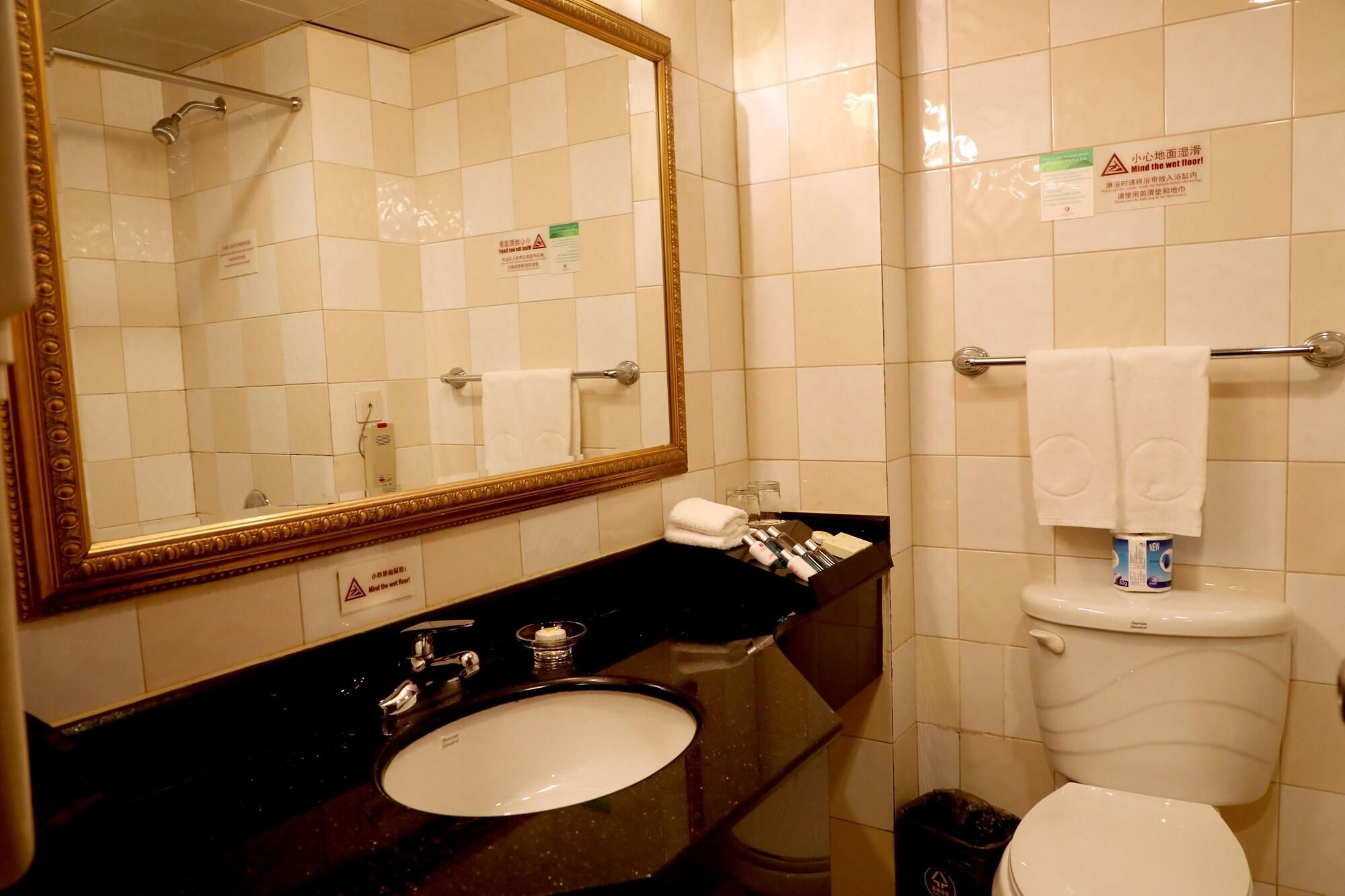 Une salle de bain avec un lavabo, un miroir et des toilettes. On y trouve des panneaux sur les murs, un porte-serviettes et une poubelle.