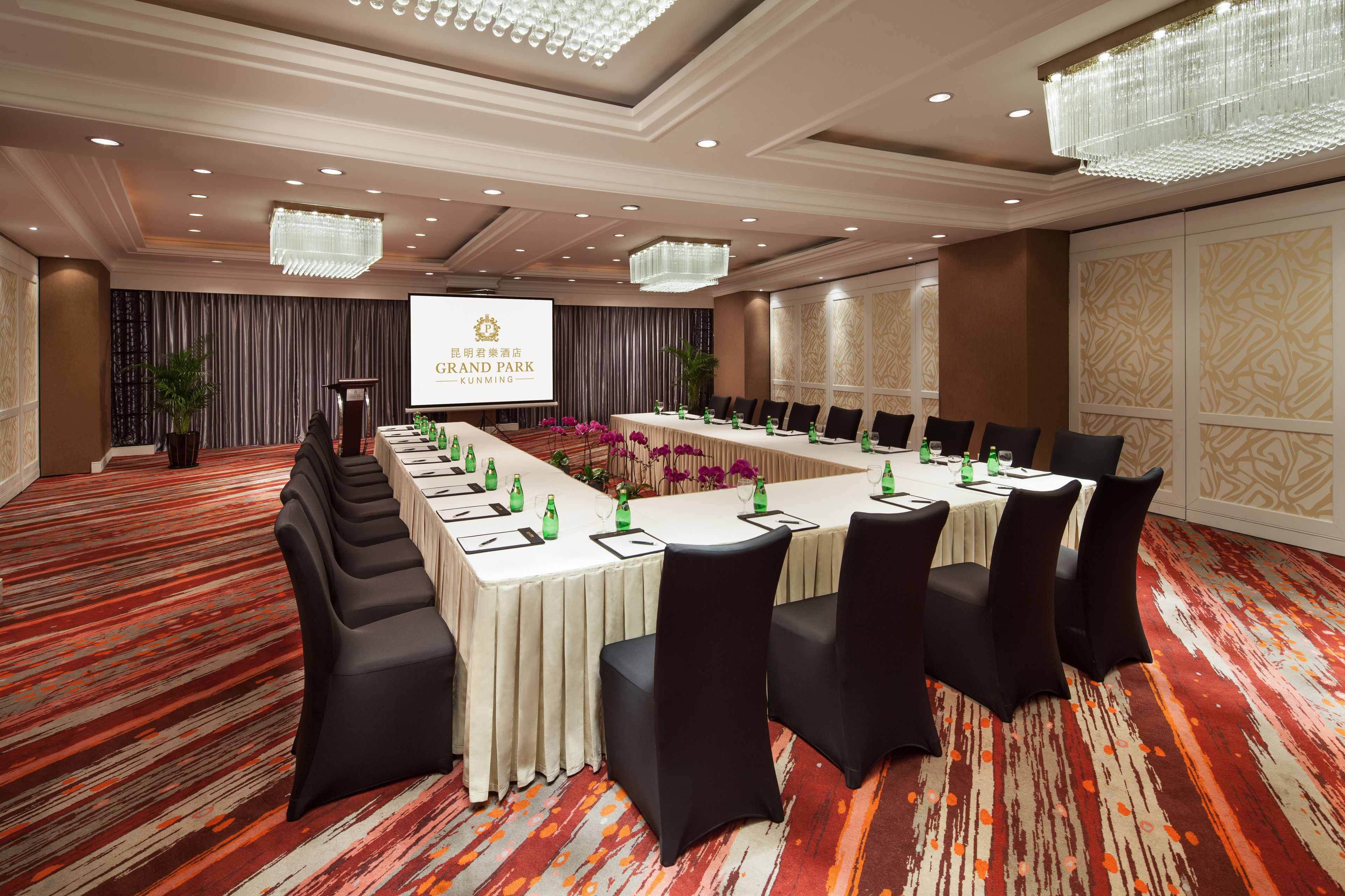 A conference room with a long table, black chairs, and a projector screen displaying the Grand Park Kunming logo.