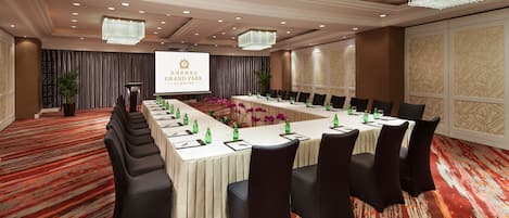 A conference room with a long table, black chairs, and a projector screen displaying the Grand Park Kunming logo.
