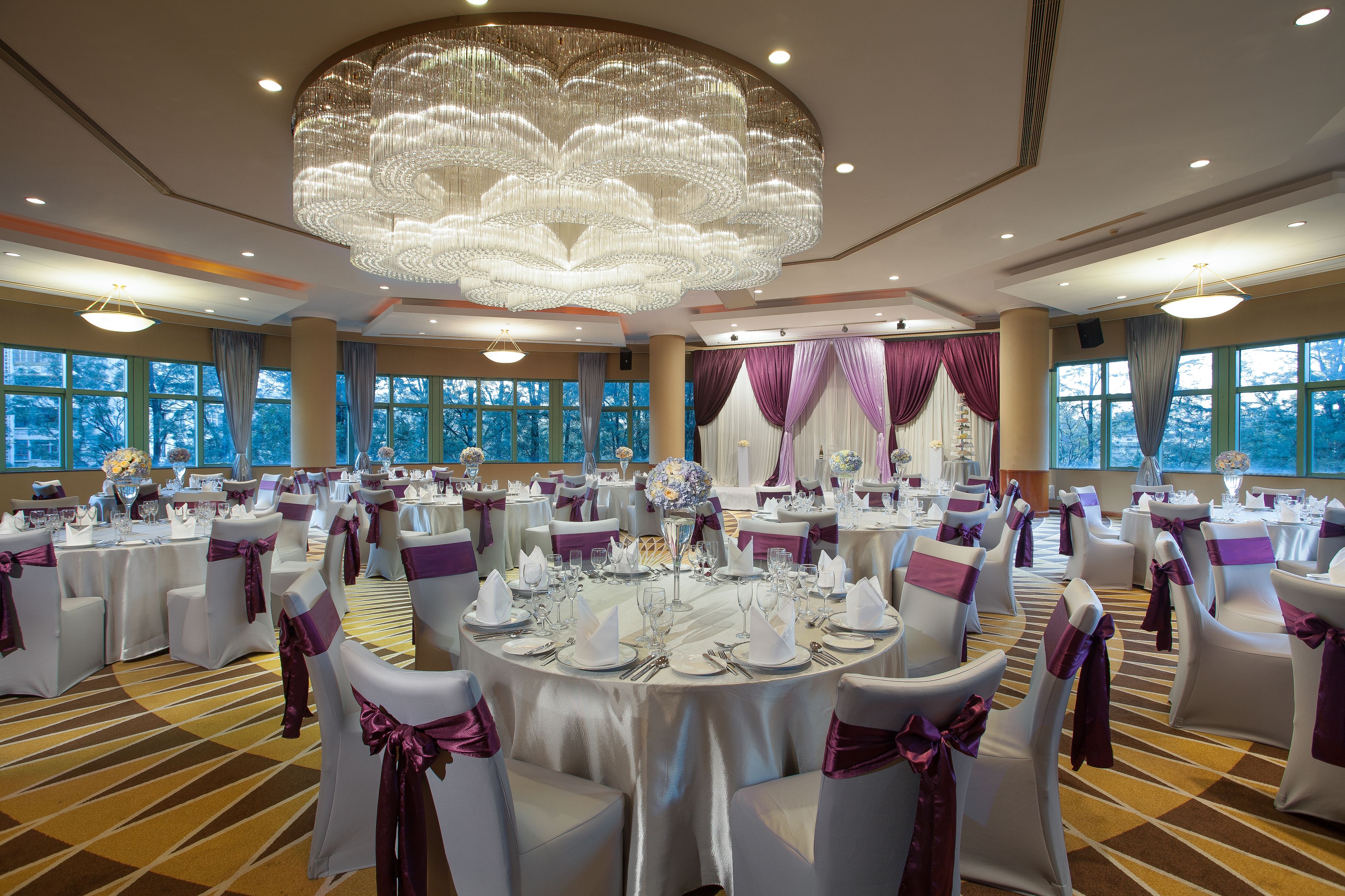 A banquet hall with round tables, white chairs with purple sashes, and a large chandelier.