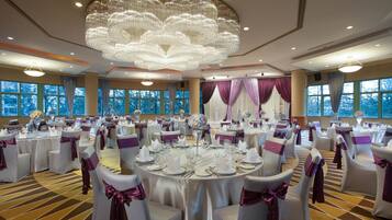 A banquet hall with round tables, white chairs with purple sashes, and a large chandelier.