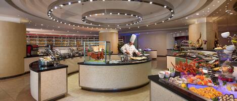 A buffet area with a chef preparing food, surrounded by various food stations and a well-lit ceiling design.