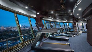 Un gimnasio con cintas de correr y equipamiento de ejercicio, amplias ventanas con vista a la ciudad y un diseño arquitectónico moderno.