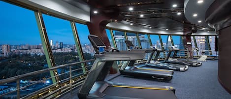 A gym with treadmills and exercise equipment, large windows with a city view, and a modern architectural design.