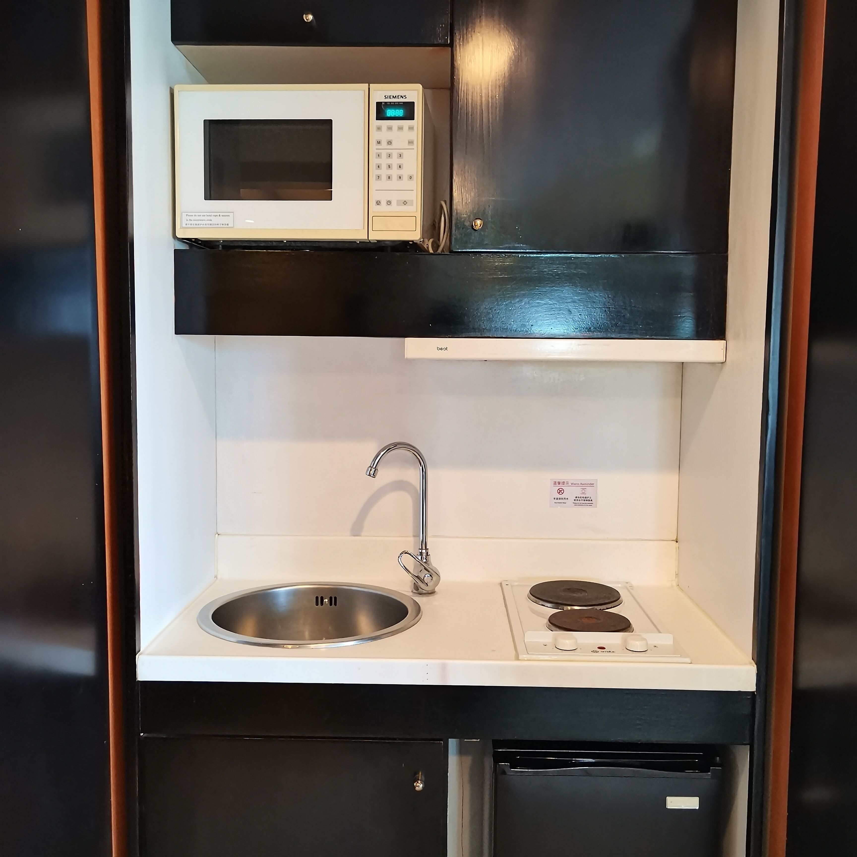 A compact kitchenette with a microwave, sink, and stove.