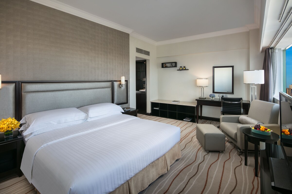 A hotel room with a large bed, a desk, a chair, and a small table with fruit.