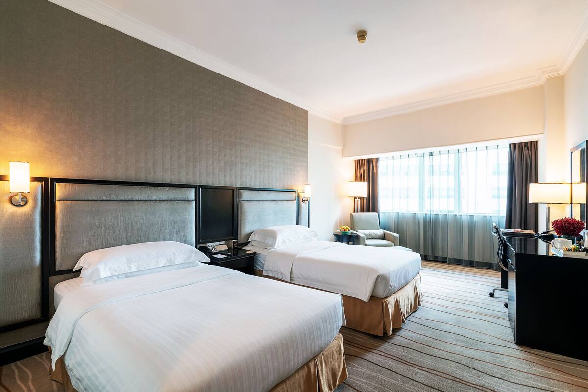 A hotel room with two beds, a desk, a chair, and a large window with curtains.