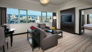 Habitación de hotel con vistas a la ciudad, televisor de pantalla plana, sofá, mesa de centro y zona de comedor.